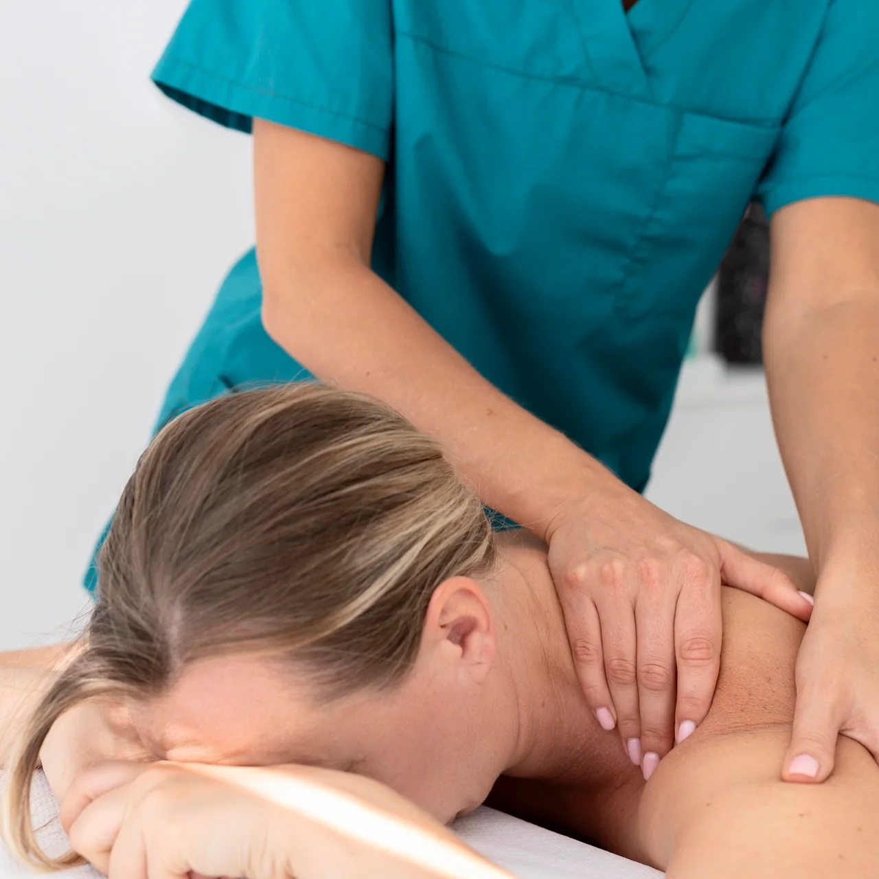 La fisioterapista lavora con le mani sulle spalle di una paziente distesa sul lettino