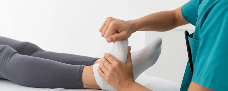 Le mani della fisioterapista muovono la caviglia di una paziente distesa sul lettino
