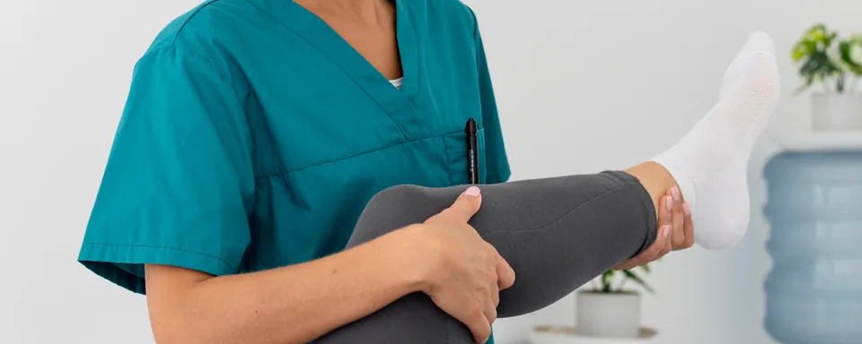 Le mani della fisioterapista accompagnano il ginocchio piegato di una paziente distesa sul lettino