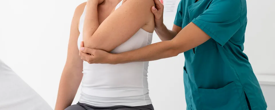 La fisioterapista muove la spalla di una paziente seduta, con una mano sull'articolazione